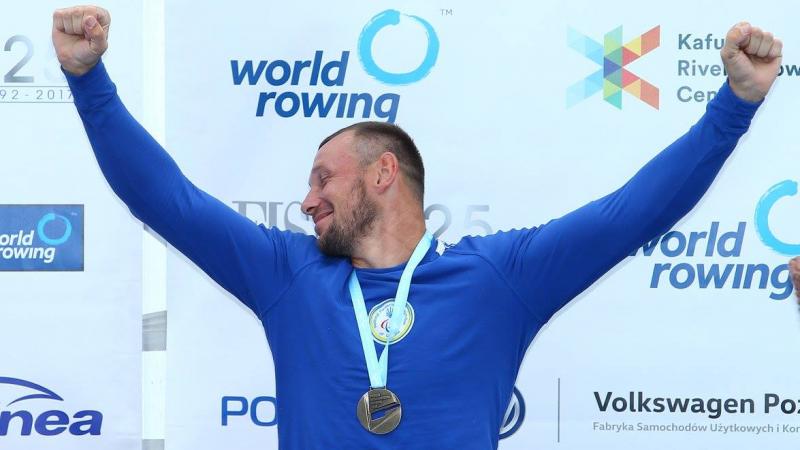 rower raises arms to celebrate gold medal on podium
