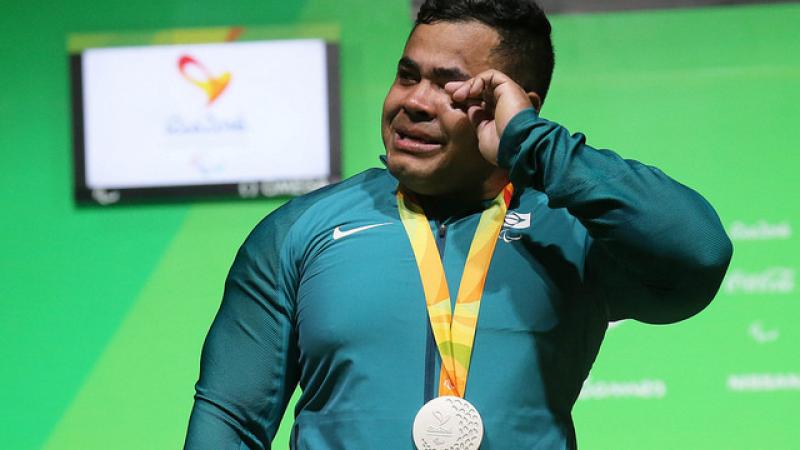 man cries while holding silver medal on podium