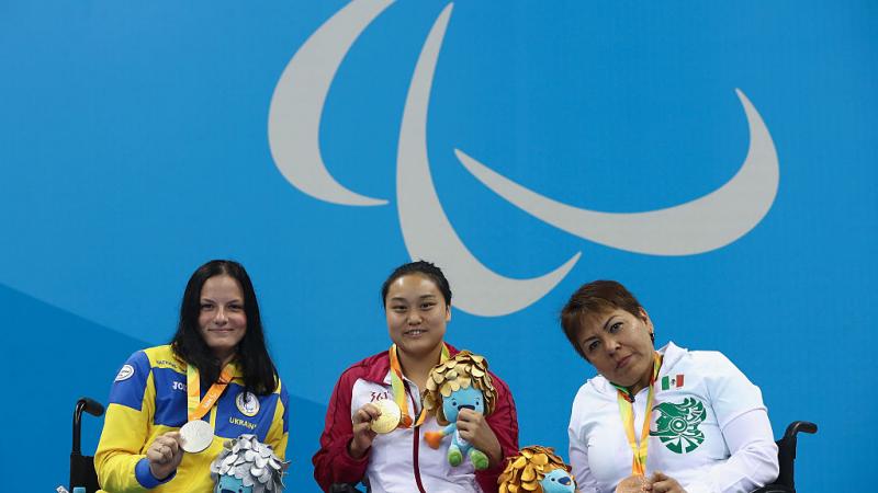 three women in wheelchairs holding medals on a podium