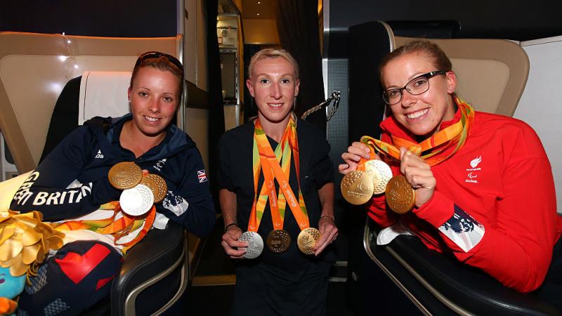 three women on a plane holding their Paralympic medals and smiling