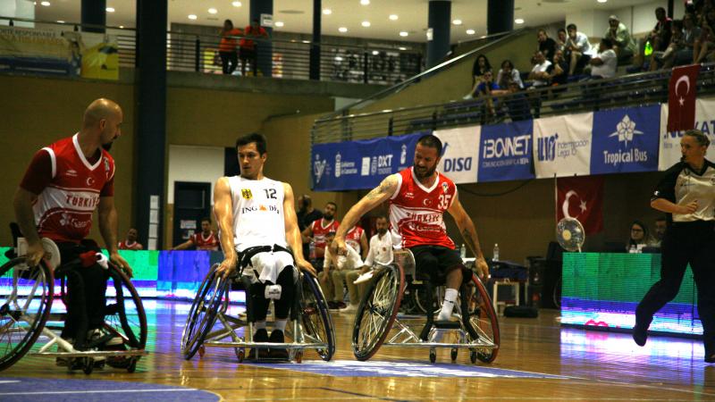 a group of men in wheelchairs challenge for a basketball