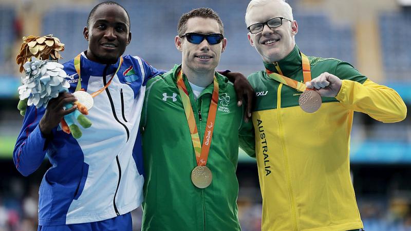 three men stand on a podium with their medals