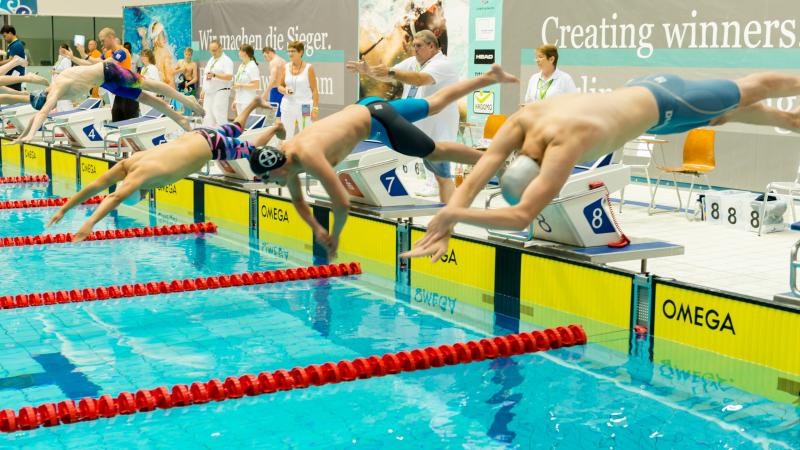 a group of male swimmers dive into the pool at the start of the race