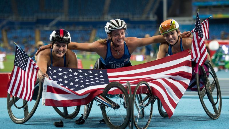 three female wheelchair athletes hold up the American flag