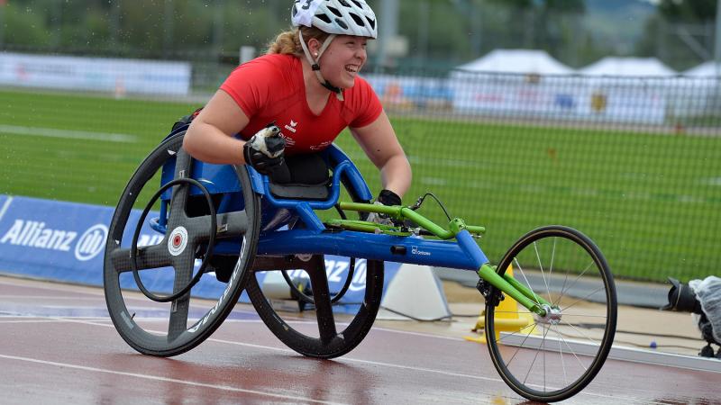 Athlete in a wheelchair celebrates clencing her first with a big smile on a wet track.