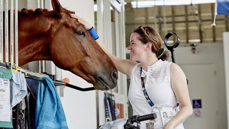 a para equestrian rider pats her horse in the stables