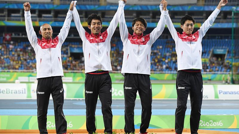 a group of four male Para athletes raise their arms in celebration