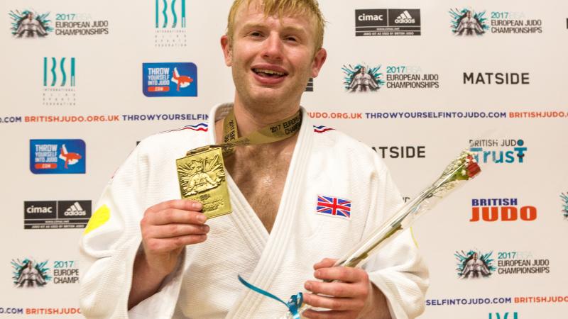 a man holds up his gold medal and smiles