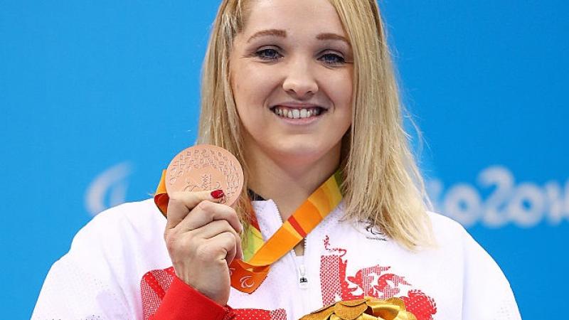 a woman holds up her medal and her mascot