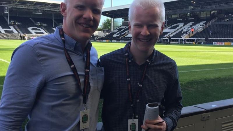 two men smile at the side of a football pitch