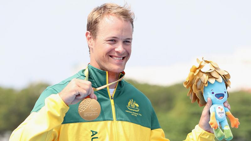 a man holds up his gold medal on the podium