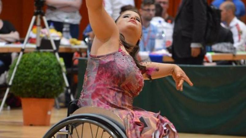 a para dancer in a wheelchair raises her arms