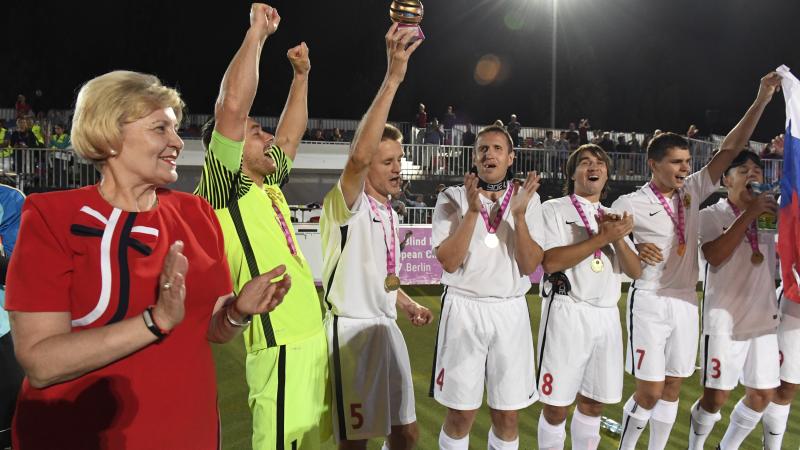 a group of male blind footballers raise their arms in celebration