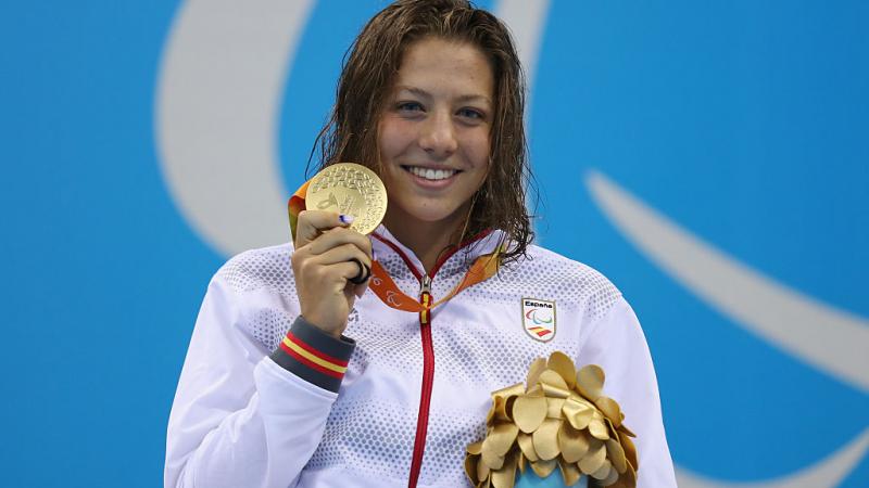 a female Para swimmer holds up her gold medal