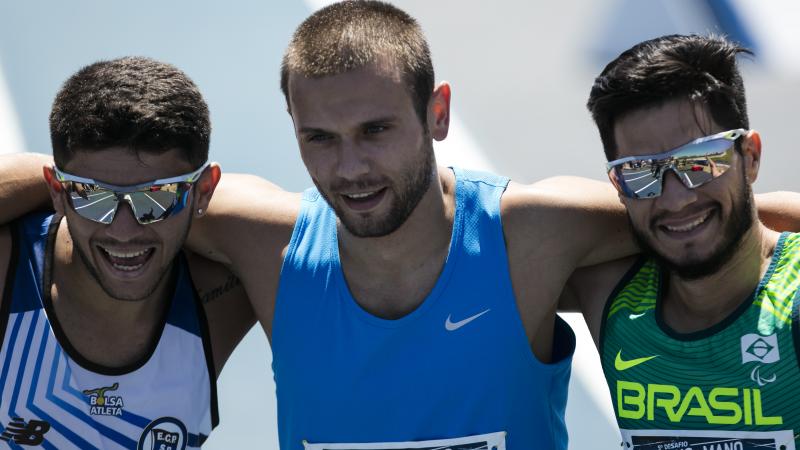 three male Para sprinters hug on the finish line