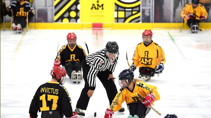 a group of Para ice hockey players take instruction from a referee