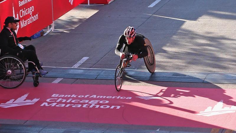 a male wheelchair racer crosses the finish line