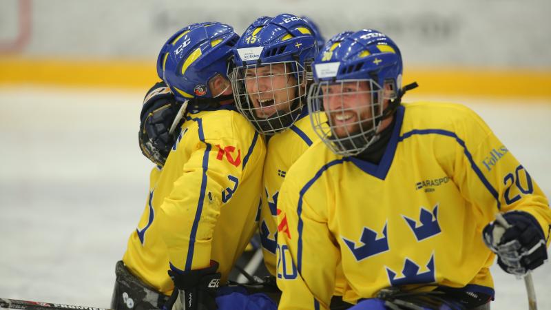 a group of Para ice hockey players hug on the ice