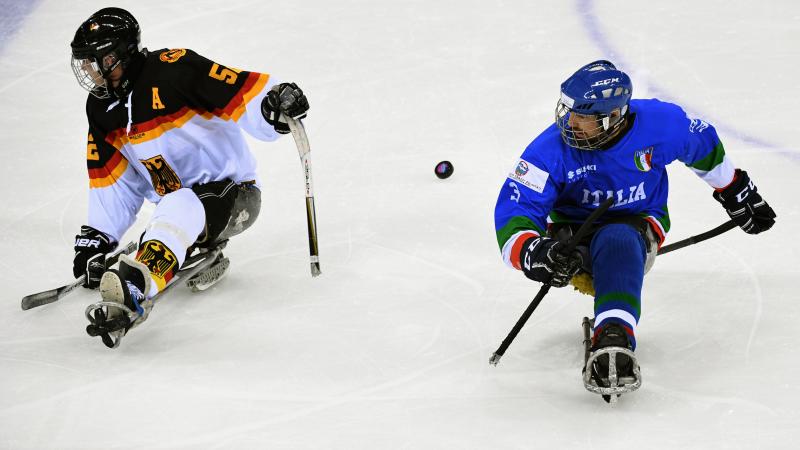 two male Para ice hockey players contest a puck