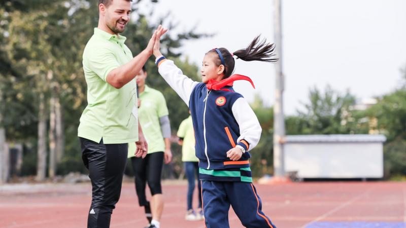 a male Para athlete high fives a girl on the track