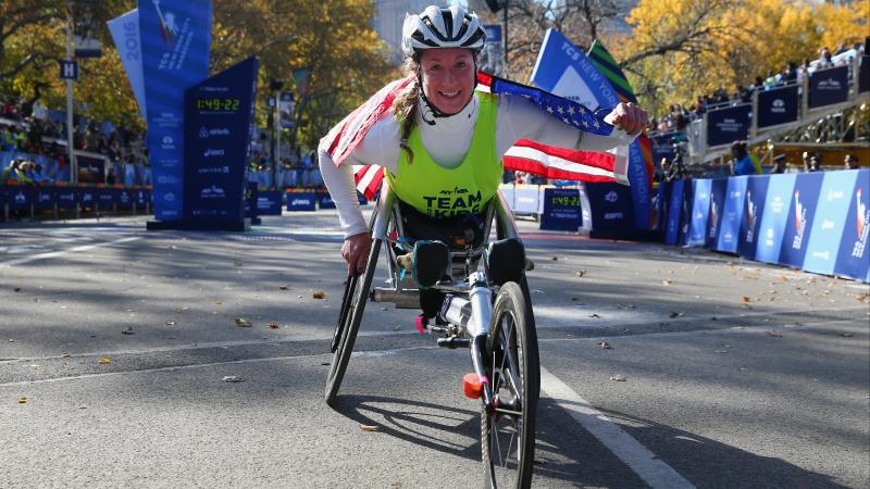 a female Para wheelchair racer celebrates with an American flag