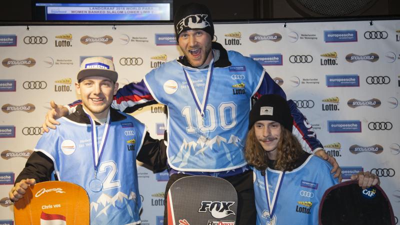 Three male snowboarders pose on podium