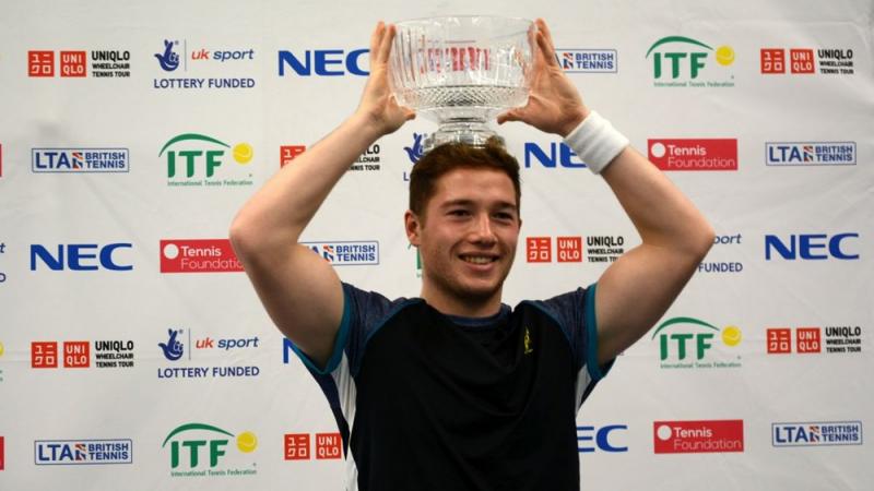 A male wheelchair tennis player lifts a glass trophy