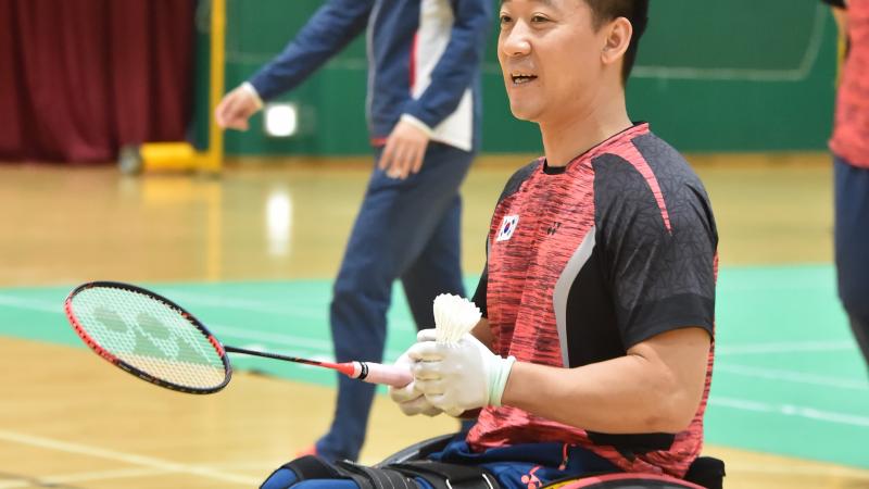 A male Para badminton player holds a shuttlecock and racquet