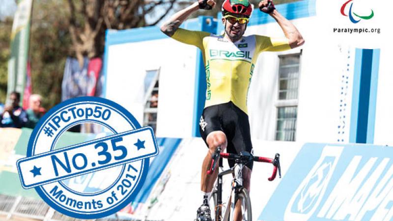 a male Para cyclist raises his arms in celebration as he crosses the finish line