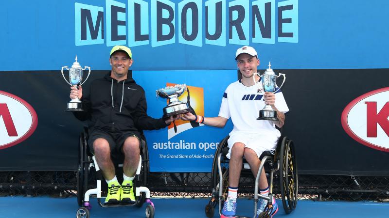 two male wheelchari tennis players hold up a trophy between them