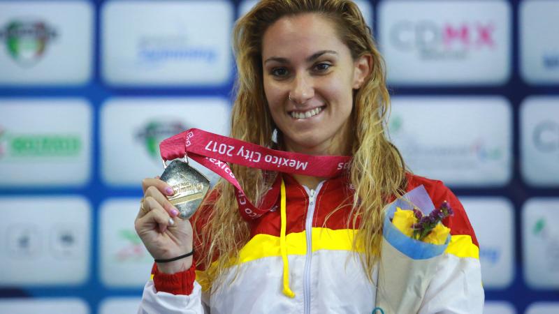 a female Para swimmer holds up her gold medal on the podium