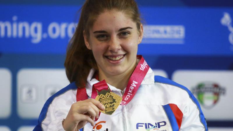 a female Para swimmer holds up her gold medal and smiles