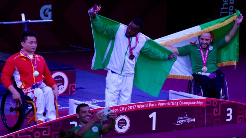 three powerlifters on the podium, two holding up flags