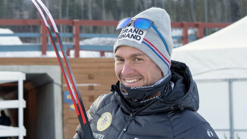 a male Para skier smiles at the camera while holding his skis