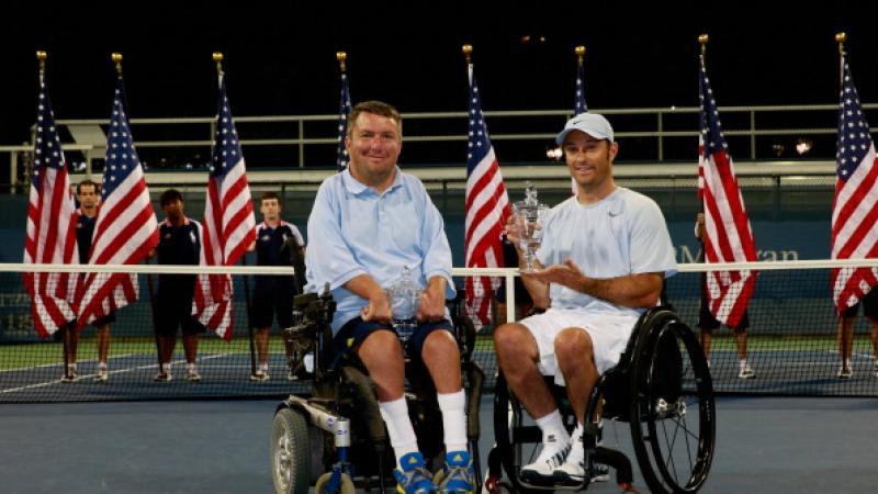Two men in wheelchairs pose for photo on tennis court