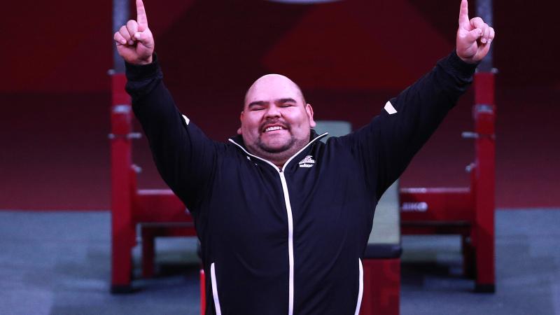 a male powerlifter raises his arms in celebration