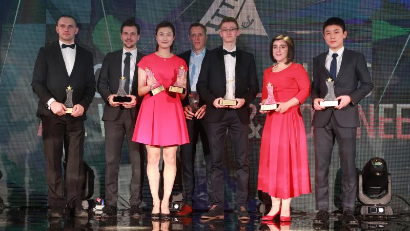 a group of men and women stand on stage with their trophies