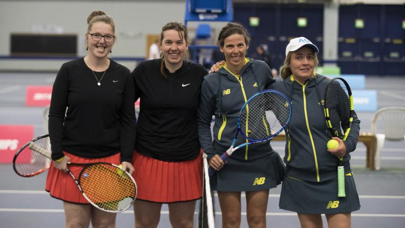 four female tennis players stand at the net