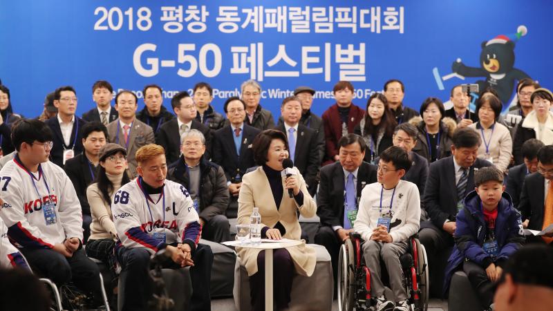 a woman speaks to a group of able bodied and wheelchair athletes