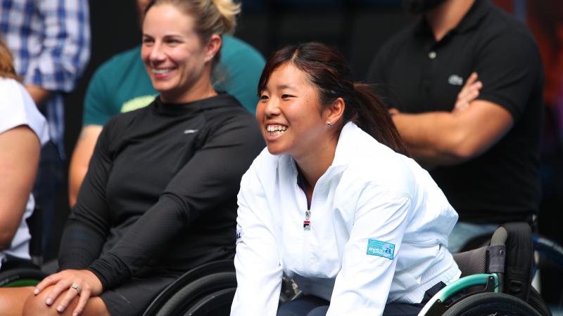 a female wheelchair tennis player smiles in delight
