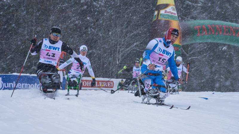 a group of male sit skiers race on the snow