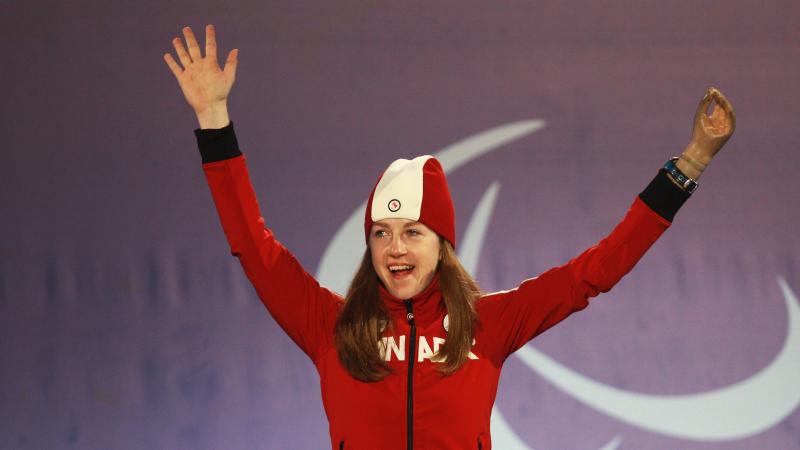 a female Para skier raises her arms in celebration on the podium