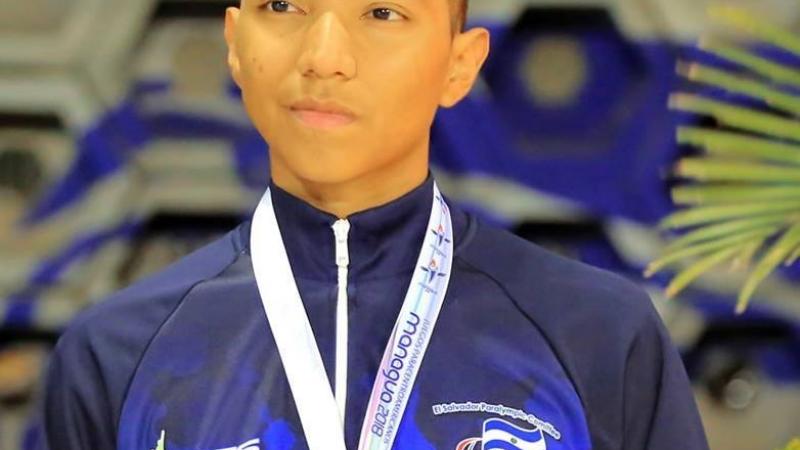 a male Para swimmer stands on the podium with a gold medal round his neck