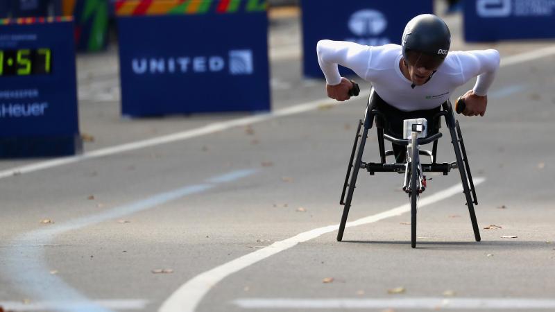 a male wheelchair racer heads towards the finish line