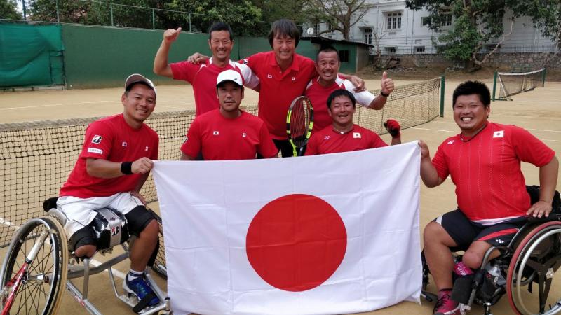 a group of male wheelchair tennis players pose with a Japanese flag