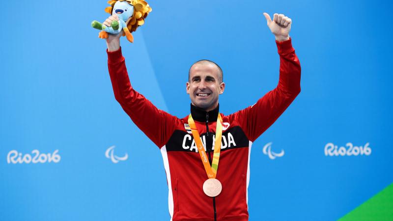a male Para swimmer raises his arms on the podium