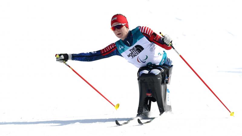 a female sit skier pushes through on the biathlon course