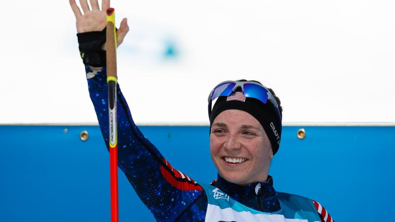 a female Nordic skier smiles and waves 