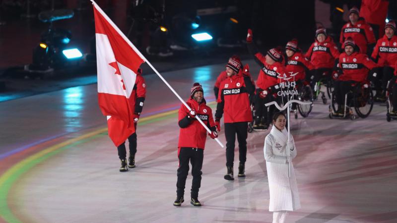 a male Para athlete carrying the Canadian flag