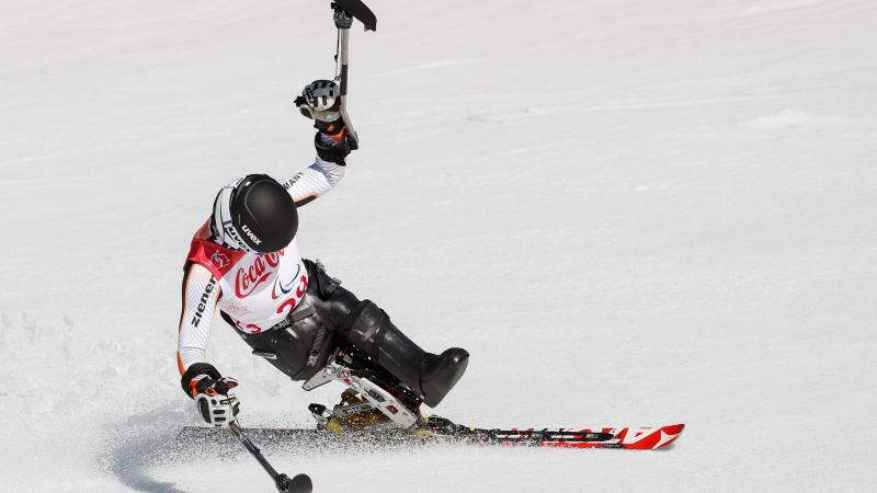 a female sit skier celebrates with her ski in the air